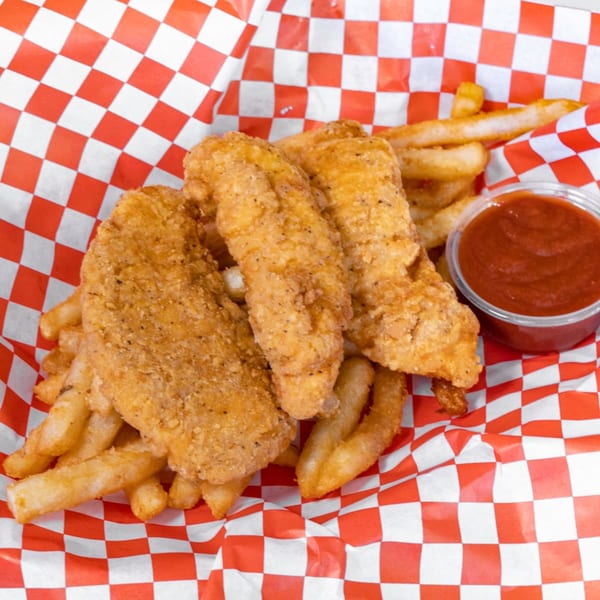 Crispy fried chicken tenders and french fries with a side of ketchup in a red and white checkered basket.