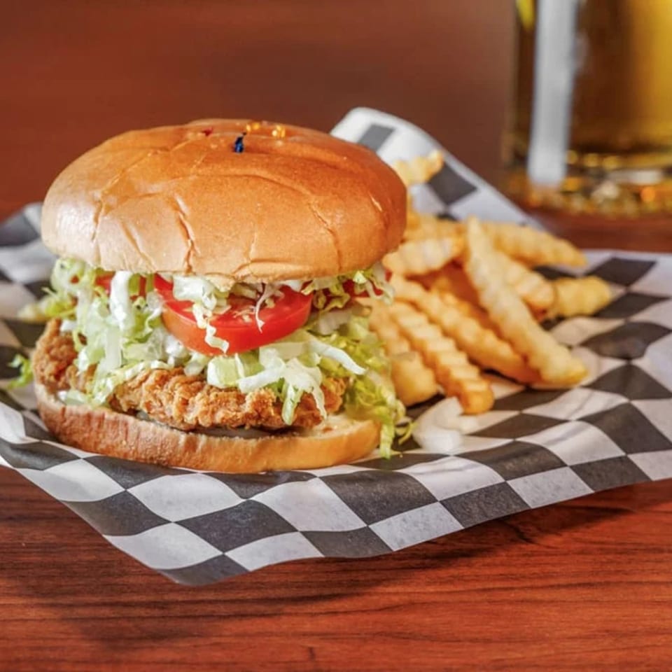 Crispy chicken sandwich with lettuce, tomato, and sauce, served with crinkle-cut fries on checkered paper.