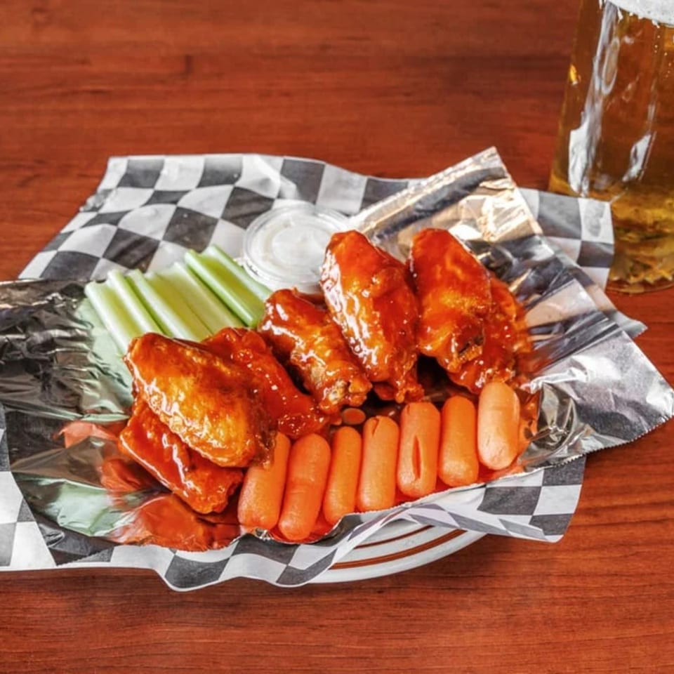 H and H Bar Grill's buffalo wings with celery, baby carrots, and ranch dressing, alongside a beer.